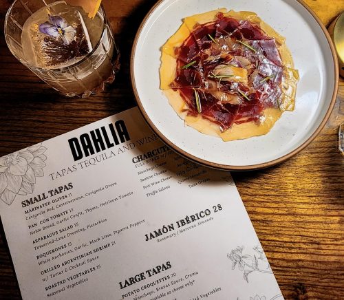 A Spanish-inspired dish next to a menu and a cocktail in a highball glass.