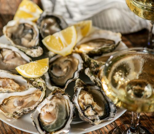 A plate of oysters with lemon wedges, next to a glass of sparkling wine.