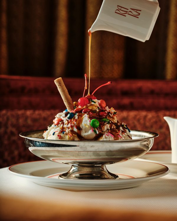 A sundae with chocolate sauce being poured over it.