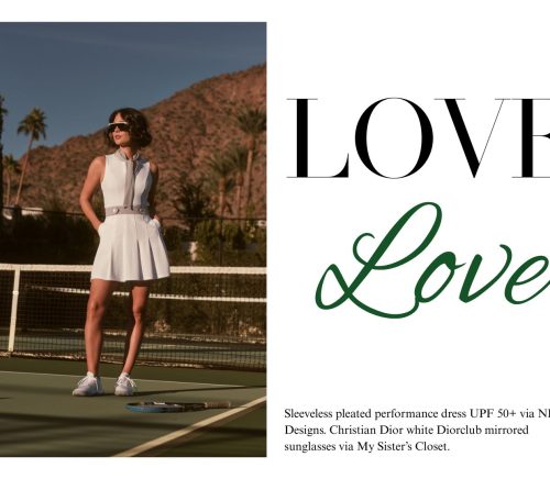 A girl standing up against a tennis net in a white tennis dress.