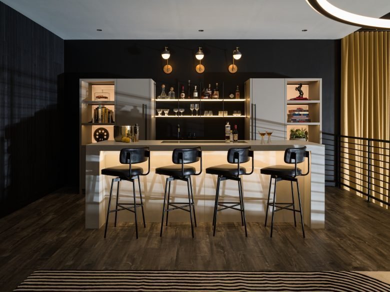 A bar at the top loft part of the garage with exposed shelving and four black barstools.