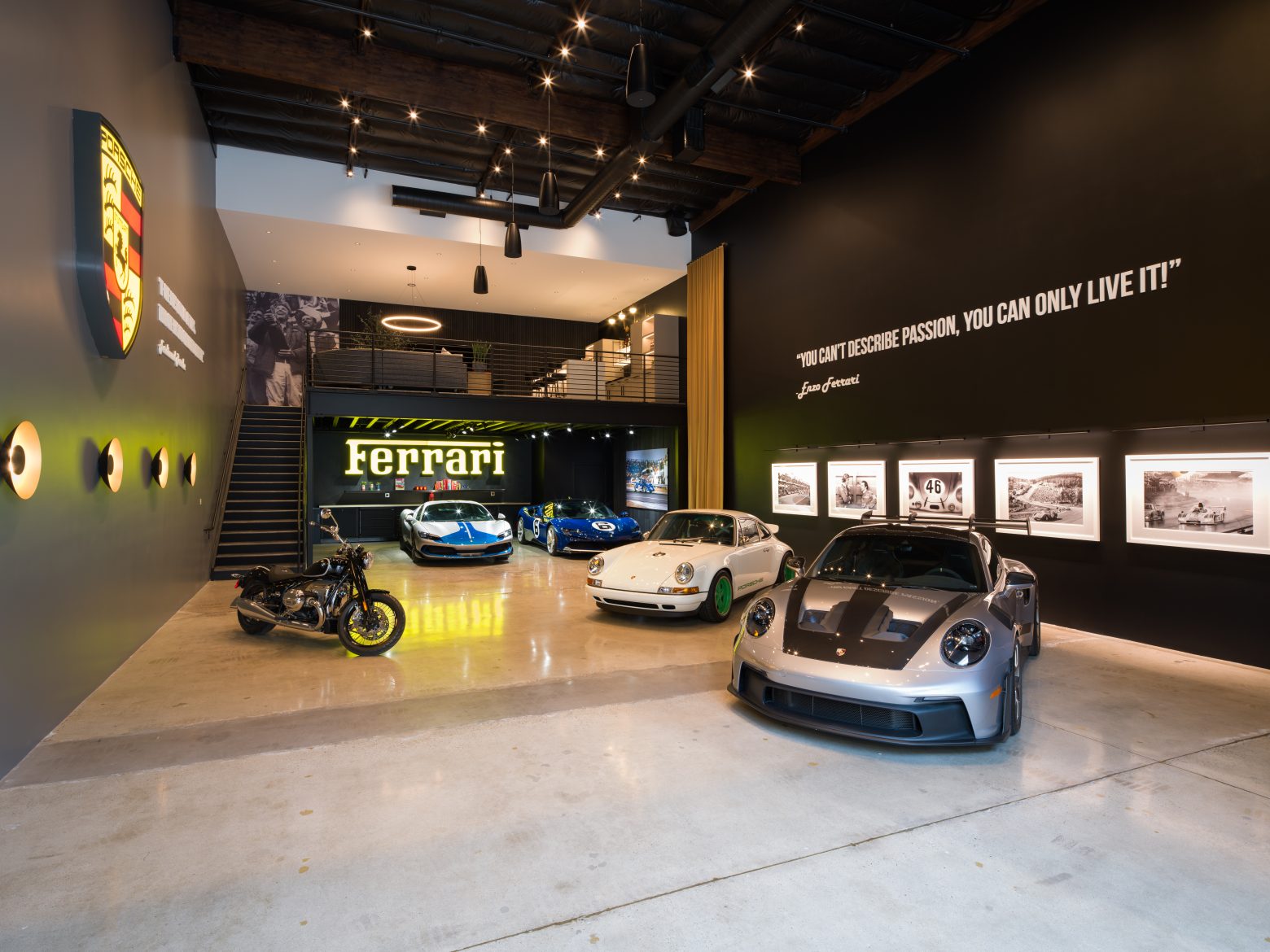 A garage with several sports car, a large Ferrari sign and a loft.