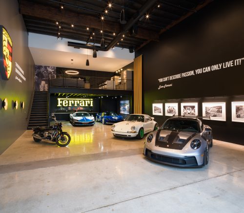 A garage with several sports car, a large Ferrari sign and a loft.