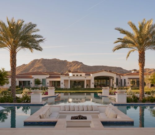 A backyard with a large pool and a conversation pit in the middle of the pool.
